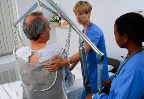 Two nurses moving a patient with a chair sling